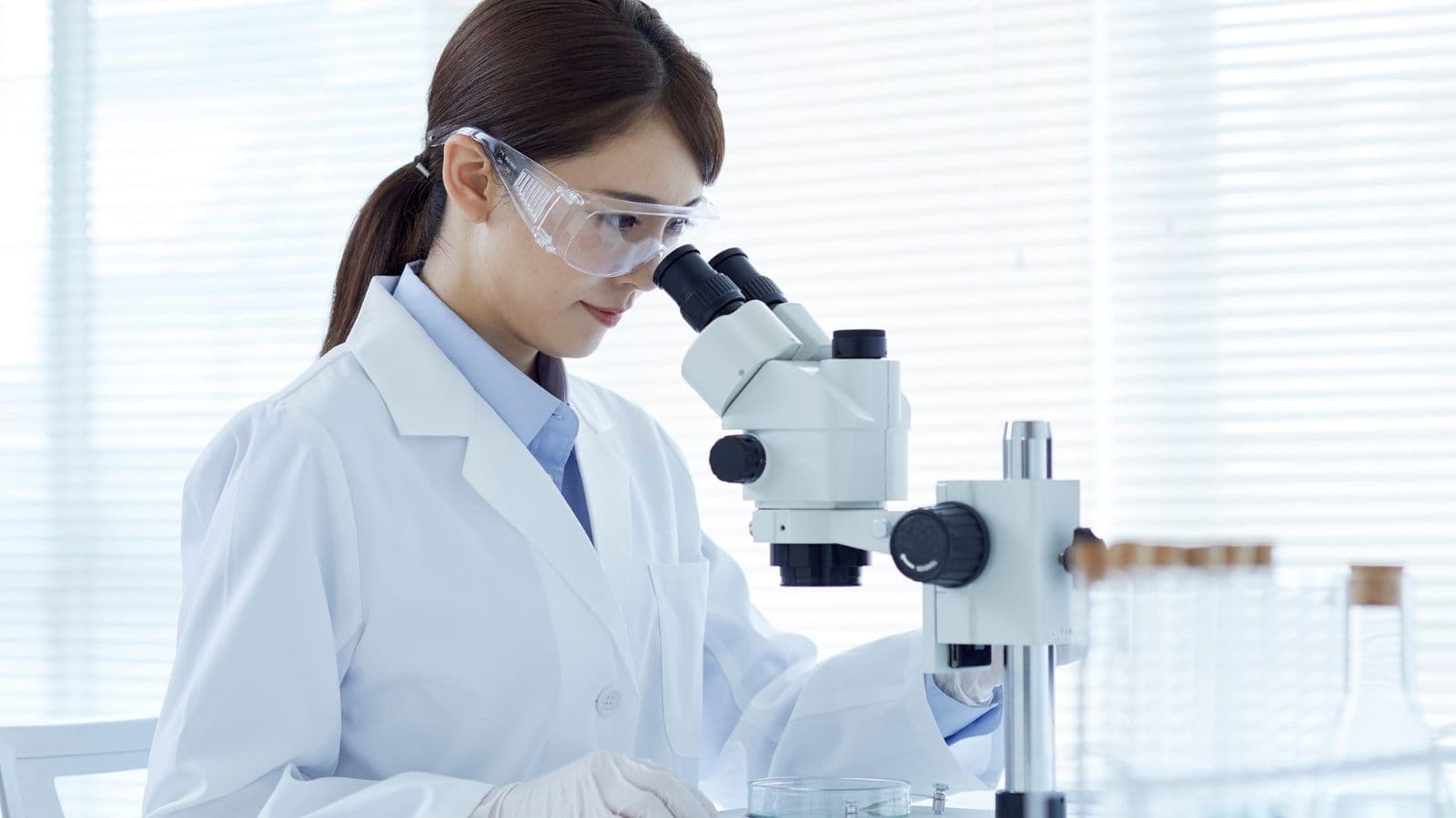 Beyaz önlüklü araştırmacı laboratuvarda mikroskopla çalışıyor